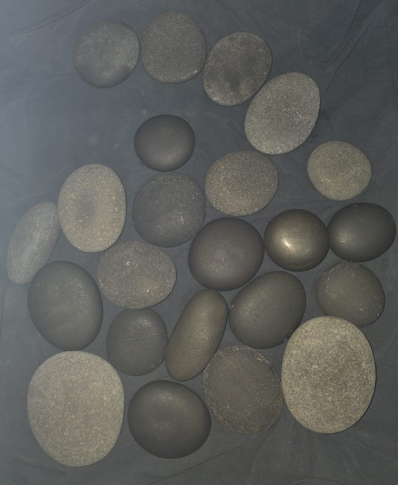 Heated black basalt stones on a dark cloth, ready for a hot stone massage in Barbados